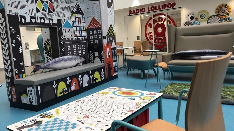 colourful tables and chairs inside a hospital sitting area with radio lillipop sign in the background.