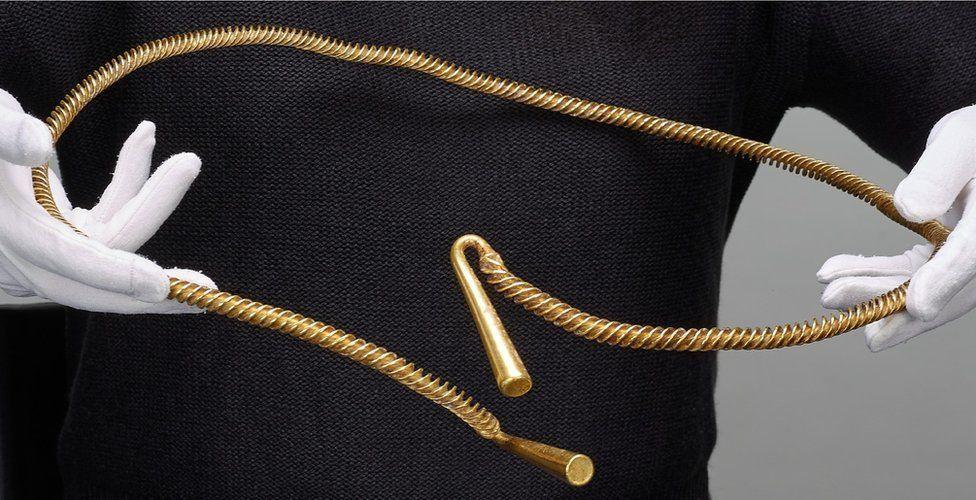 Bronze Age torc found in Cambridgeshire being held by a person wearing white gloves