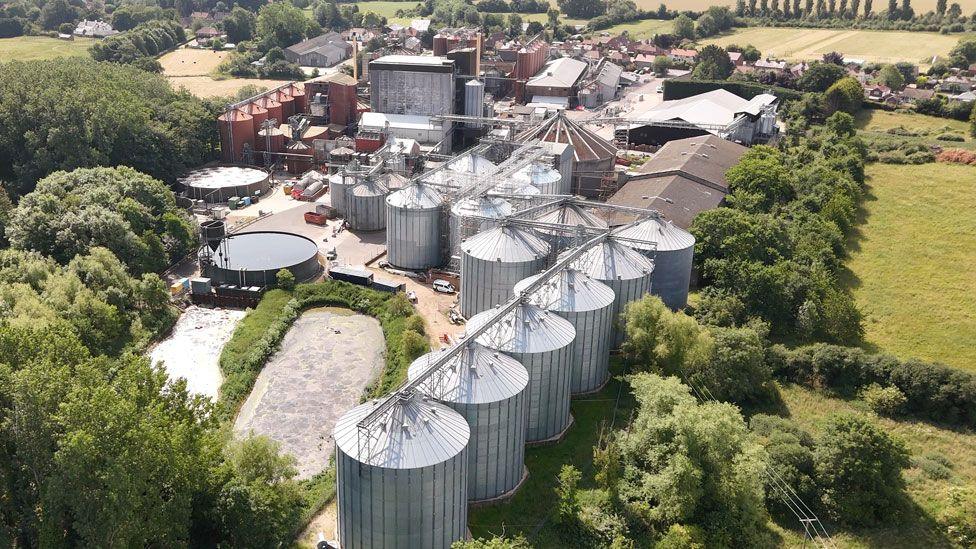 An aerial shot of Crisp Malt at Great Ryburgh. The site includes huge silver-coloured round industrial buildings as well as other industrial buildings. The site is ringed with trees and fields and houses can be seen beyond the main complex.