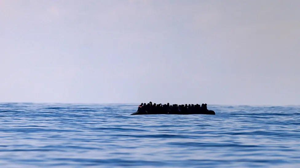 A small boat crowded with people floats in the sea