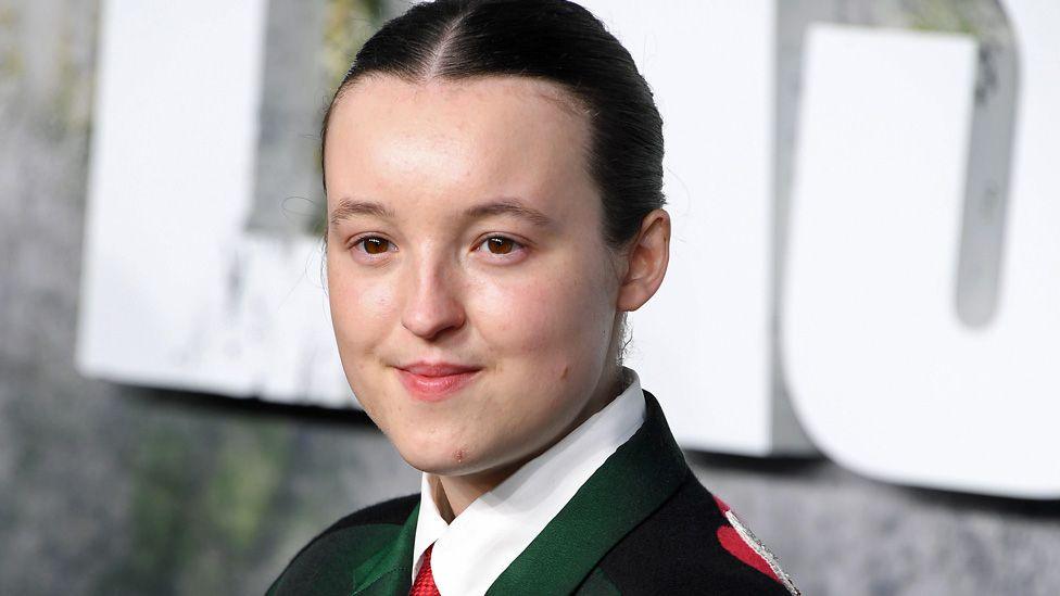 Bella Ramsey at the Last of Us premiere wearing a dark green suit and red tie
