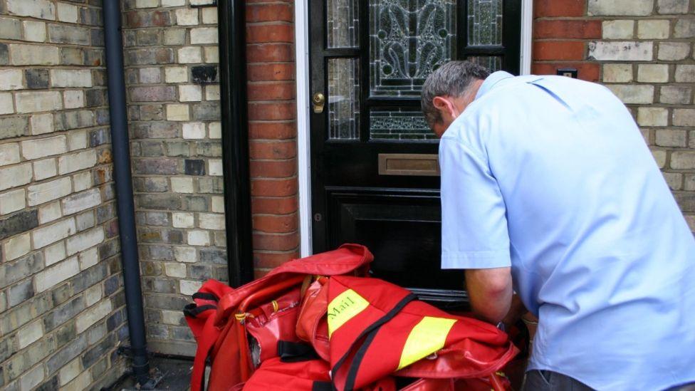 Royal Mail postman with red and yellow sack of items outside a front door