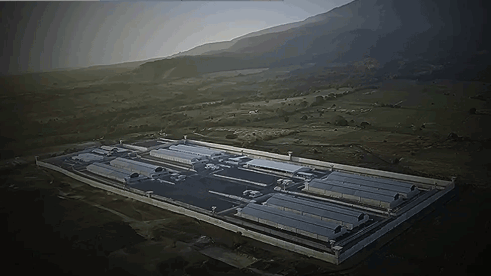 An aerial view shows the prison compound surrounded by high walls and watchtowers.