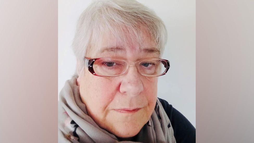 Linda Ratter, woman with grey hair and glasses looking at camera