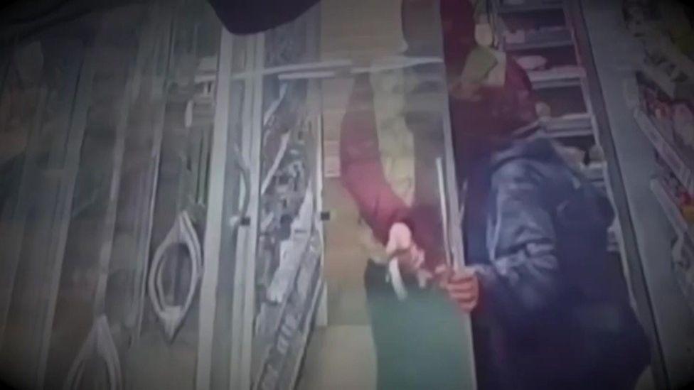 CCTV still of two shoplifters with hooded coats taking items from a fridge and loading them into a bag