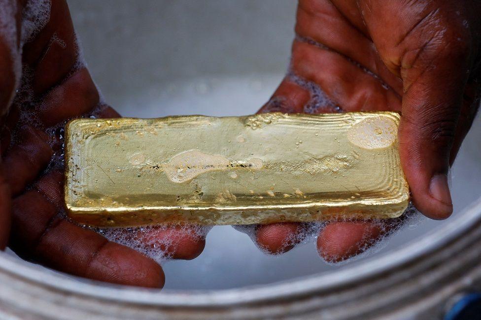 A man handles a gold bar in a wash basin.