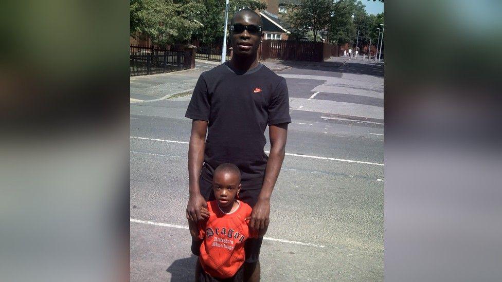 Kemoy Walker stands in a car park with holding a young Prince Walker-Ayeni's hand