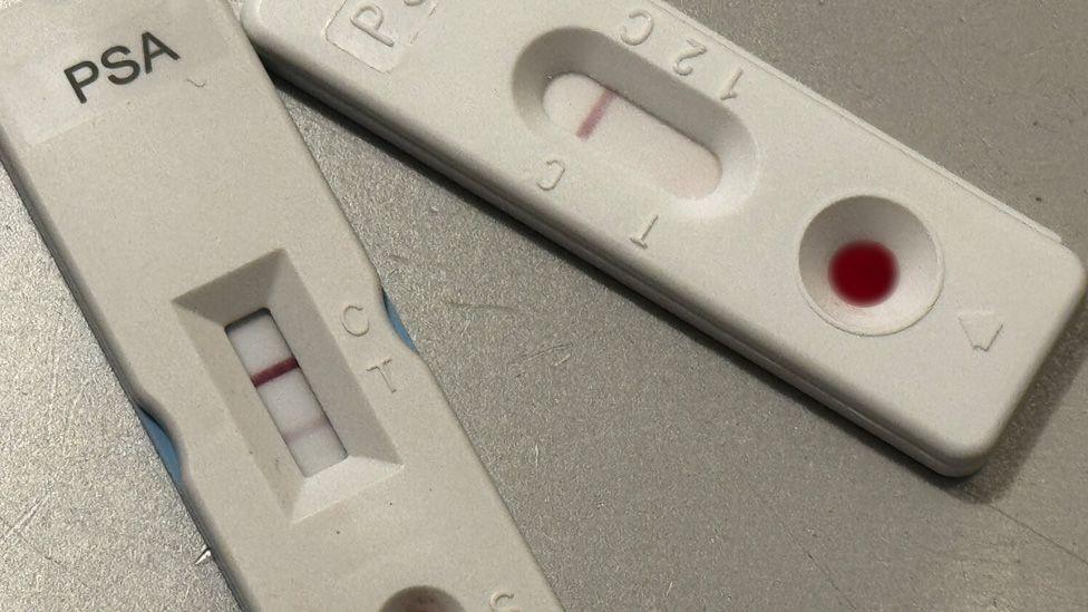 A close-up of two white PSA tests which resemble the lateral flow tests used in Covid. The test on the left shows two lines indicating a positive result. The test on the right shows just one line indicating a negative result. 
