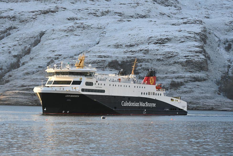 A Caledonian MacBrayne ferry in traditional blue and white colours sails across a calm sea with a frosty hill in the background