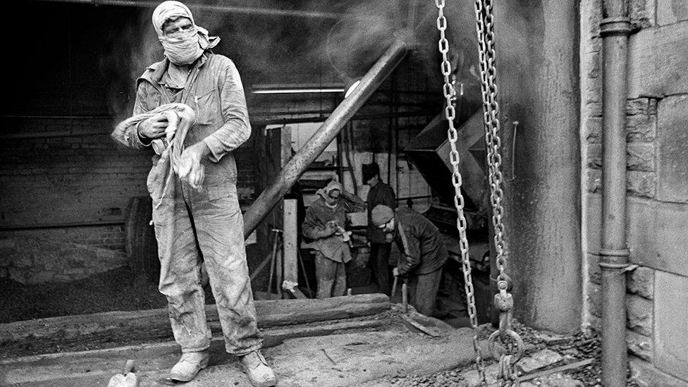 Black and white image of a worker at the mill, wearing overalls and with his hair and face covered with cloth