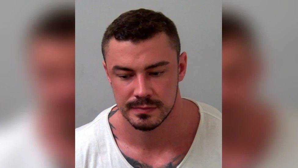 Llun heddlu o Terence Murrell wedi iddo gael ei arestio - dyn â gwallt tywyll byr, mwstash a barf fer, mewn crys gwyn sy'n amlygu tatŵ ar ei fron a'i ysgwyddau