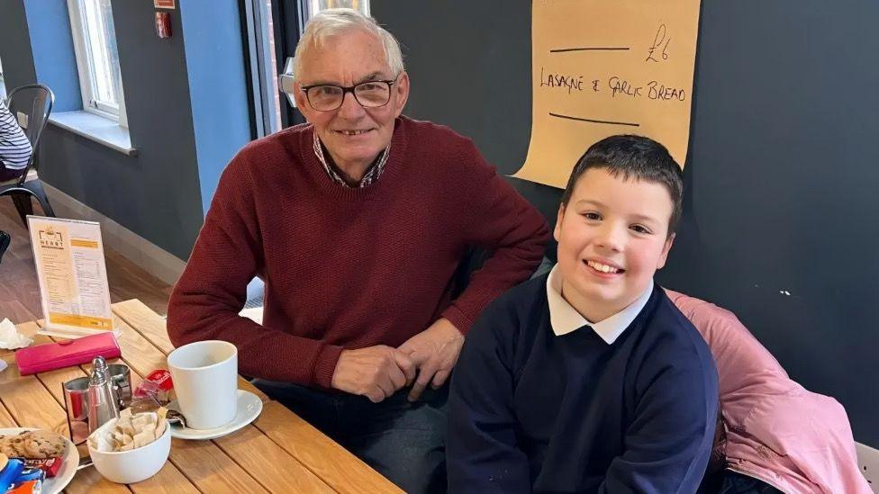 A young boy sat with an elderly man in cafe.