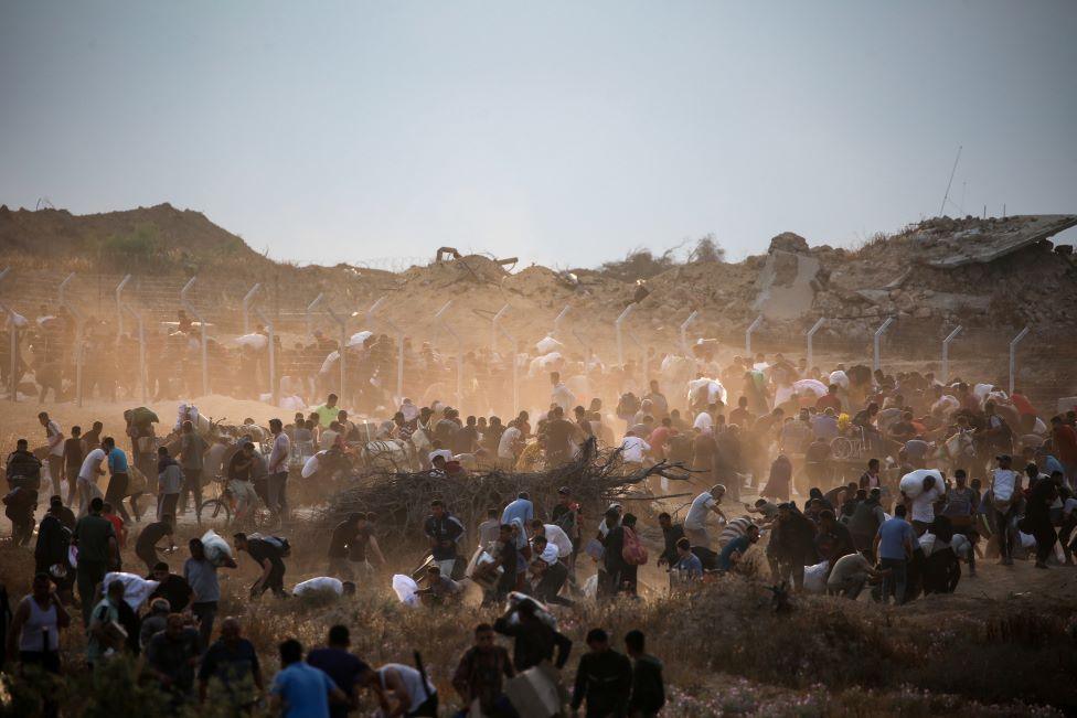 People carry relief supplies from the Gaza Humanitarian Foundation (GHF) - the picture shows lots of people, some with sacks on their backs