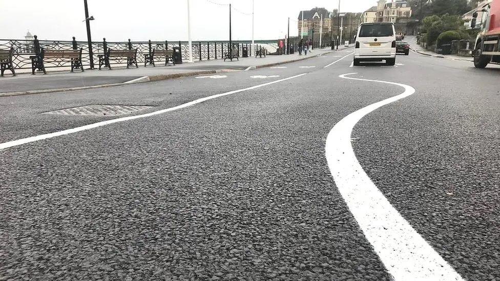 The old layout of the Clevedon seafront. There is a white wiggly line on the road. Cars can be seen on the road in the distance.