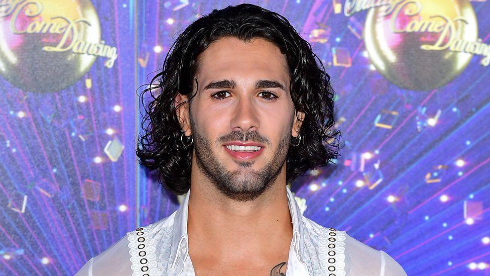 Graziano Di Prima standing in front of a backdrop showing Strictly logos and glitterballs