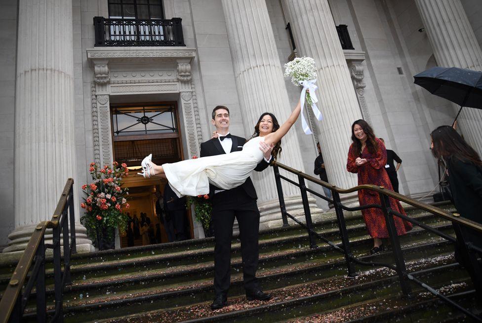 Bradley Standfield lifts his new bride, Priscilla Wong, on the steps of Old Marylebone Town Hall in central London, as the venue hosted 100 back-to-back ceremonies to celebrate its 100th birthday.