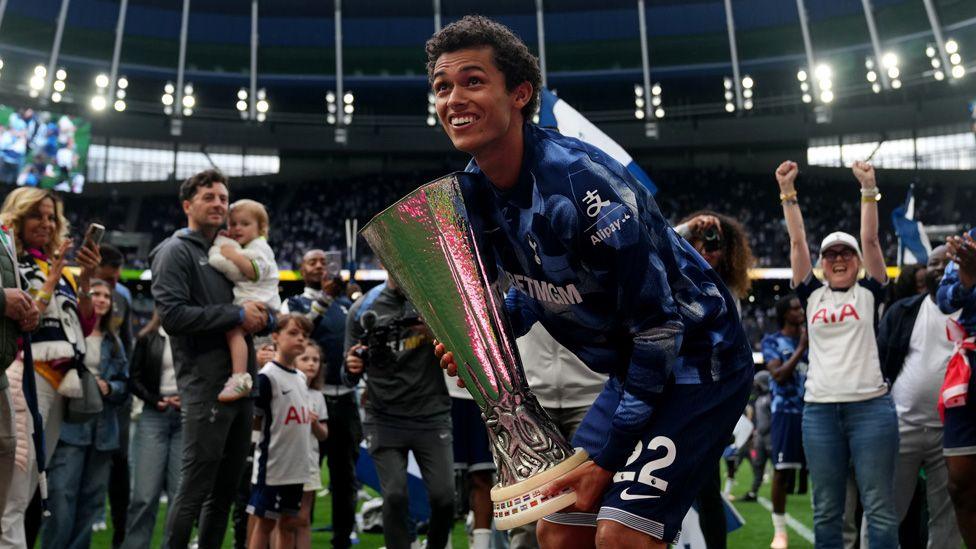 Brennan Johnson holding the Europa League trophy surrounded by people on the pitch