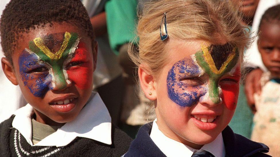 Two South African schoolchildren - one black, one white - both with a South African flag painted across their faces.