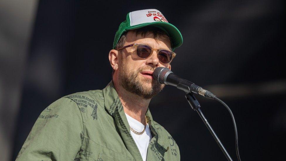 Damon Albarn pictured in a cap and sunglasses while performing on-stage at Glastonbury Festival in 2024