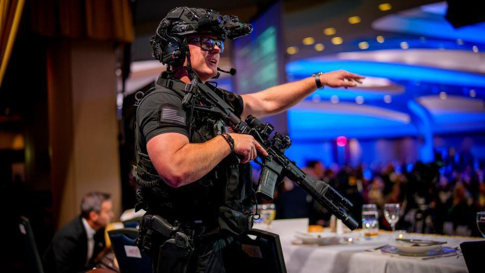 An armed Secret Service agent stands on stage following the shooting. He is dressed in black body armour and is heavily armed