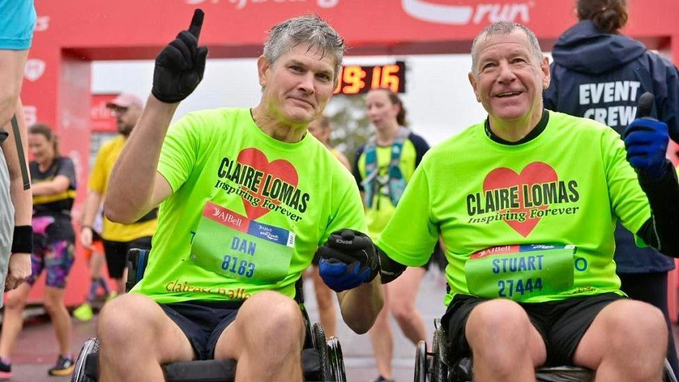 Dan Spincer and best friend Stuart Hall wearing green tops with Claire Lomas' name in front of a heart. They are sat in wheelchairs.