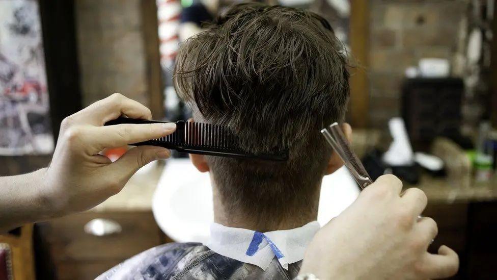 A closeup of the back of a man's head with someone combing and cutting his hair.