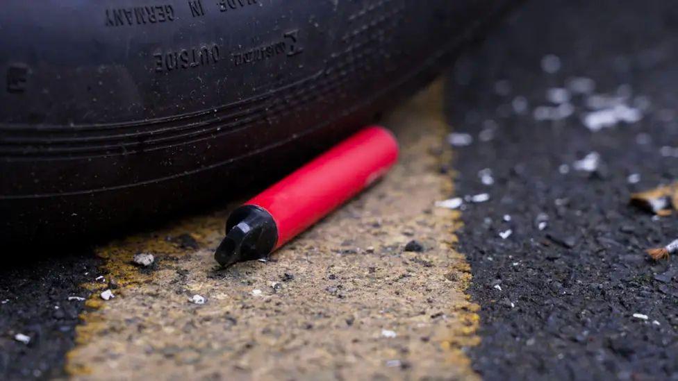 A red vape thrown away near a tyre on the road