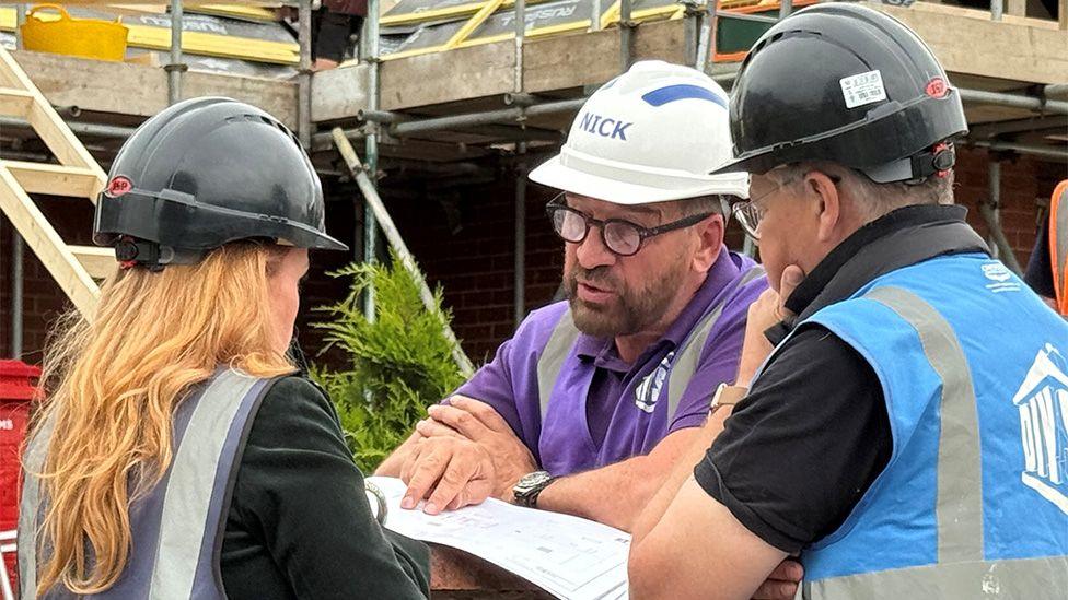 Gabby, Nick and another man looking over plans outside the house