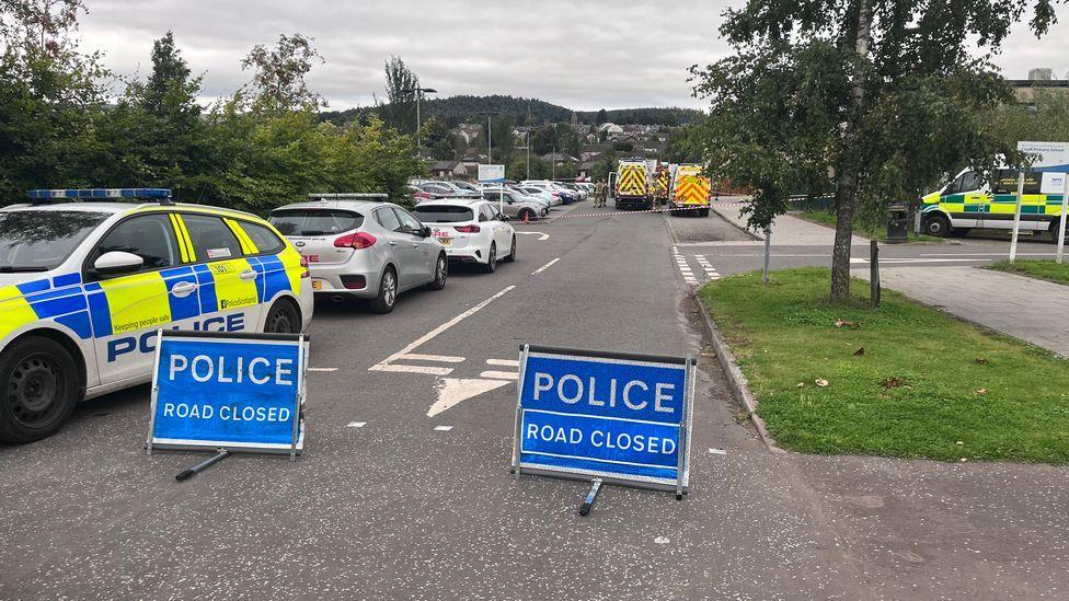 Police cars blocking the road with ambulances in background