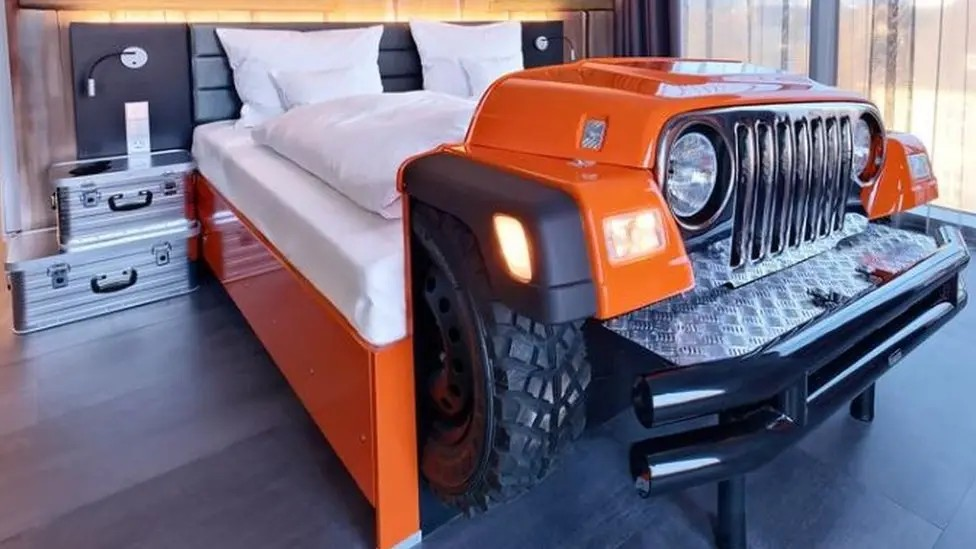 A hotel bed shaped like a car complete with wheels and headlights. 