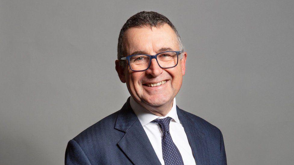 Sir Bernard Jenkin, who is wearing a suit, tie and glasses. He is smiling at the camera