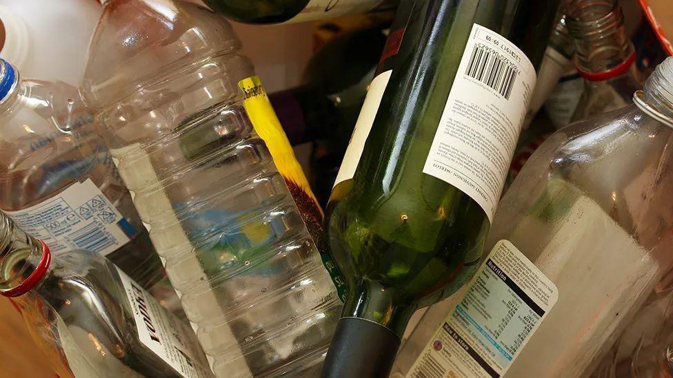 A collection of discarded empty bottles, including a green wine bottle, a plastic oil bottle and a glass bottle of vodka.