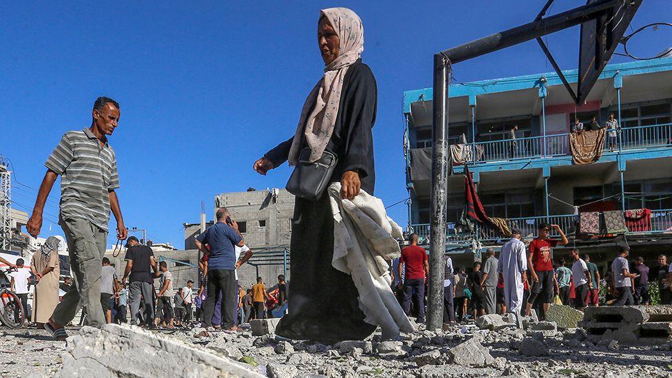 People walk over rubble next to a basketball court outside the al-Jaouni school in Nuseirat refugee camp following Israeli bombing on 11 September