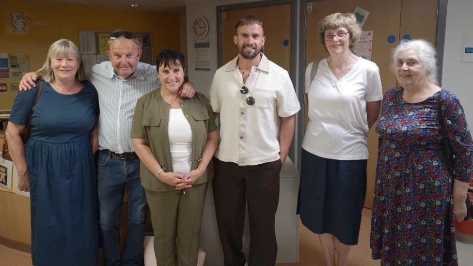 A line of six people standing alongside each other in a hospital ward and smiling. From left to right, they are: nurse Margaret Lewis, Mark and Lian Stevens, Zak Stevens, Sharon Holmshaw and Georgina Mason. 