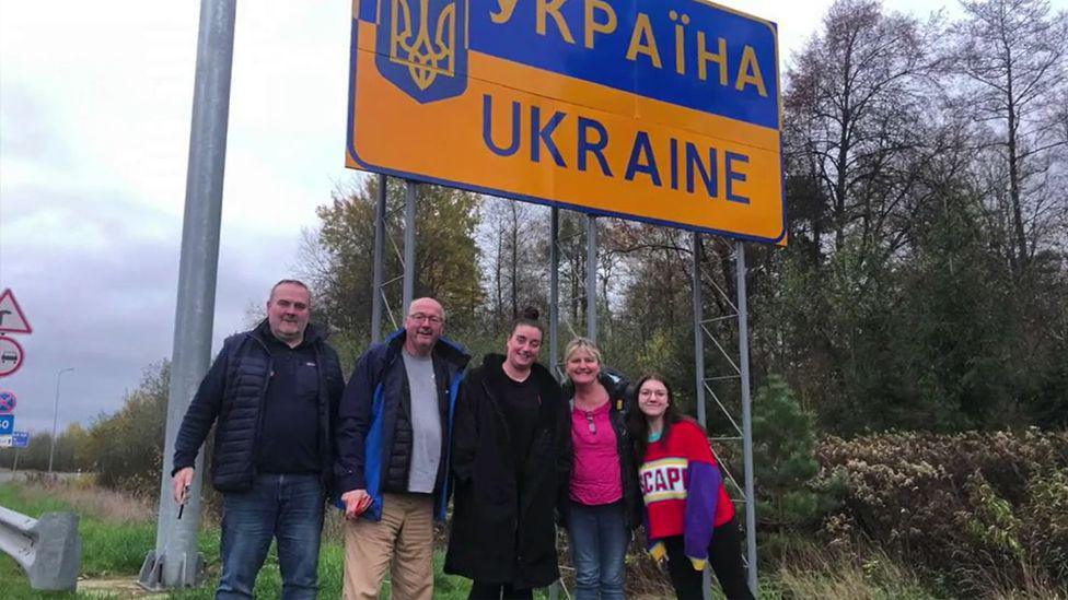 Jeanette and Craig Rice stood in front of a sign for Ukraine with two women and a man.