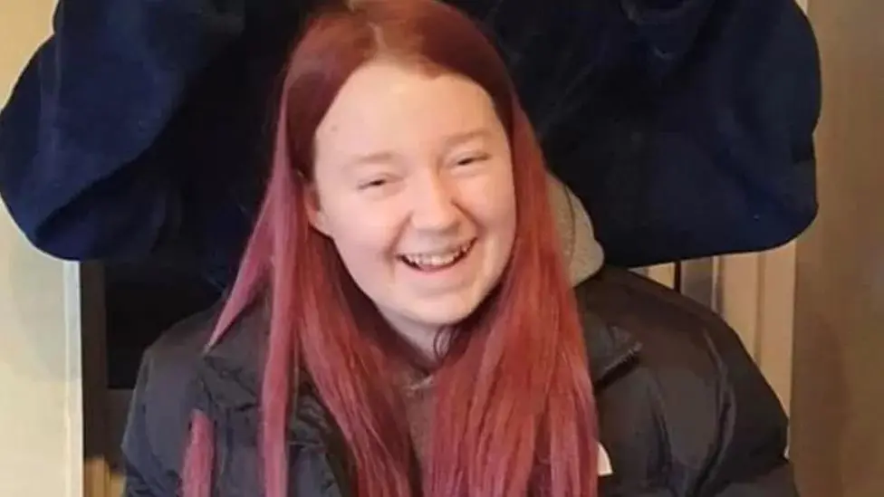 Teenage girl with pink care and black jacket. She is smiling at the camera. 