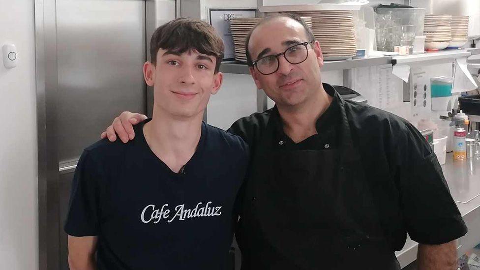 Robert Del-Rio with his father Jorge Del-Rio, who has his arm around his son's shoulder, standing in a restaurant kitchen