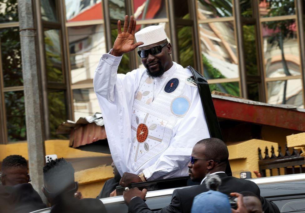 Guinean leader Mamadi Doumbouya in a smart, embroidered white boubou and dark sunglasses waves after submitting his candidacy at the Supreme Court a Conakry, Guinea, Monday 3 November 2025.