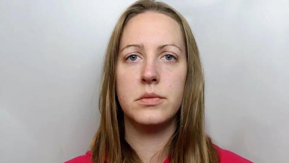 Police custody photograph of Lucy Letby who has long blonde hair and is wearing a red top.