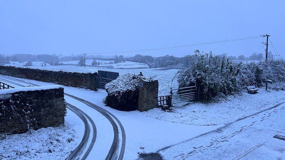 Tyre tracks in snow with snow covered fields and walls and gates leading into fields.