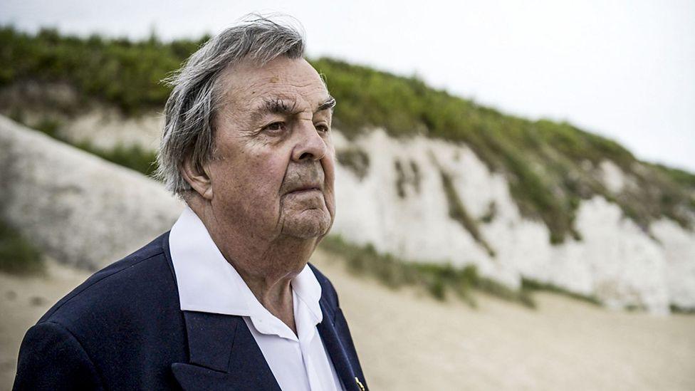 John Folkes looks out to sea, white cliffs behind him. 