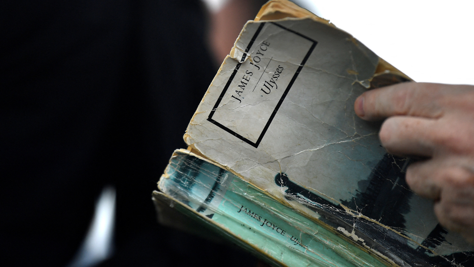 A man holds a tattered old copy of Irish author James Joyce's Ulysses.