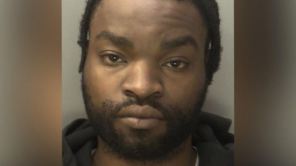 Jalen Denny is seen in a police mugshot. He is wearing a dark top and looking at the camera.
