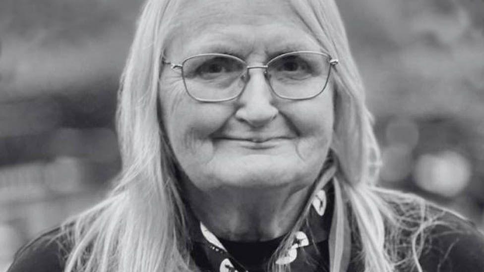 Black and white head and shoulders of Jennifer Turner in her scour uniform, with long fair hair and wire framed glasses
