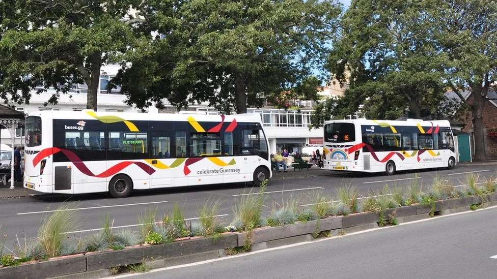 Two white buses with red and yellow livery next to a bus terminus