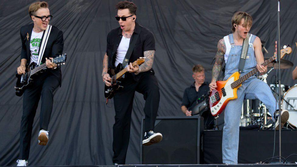 Tom Fletcher, Danny Jones and Dougie Poynter of McFly with their left legs raised playing at the Isle of Wight Festival