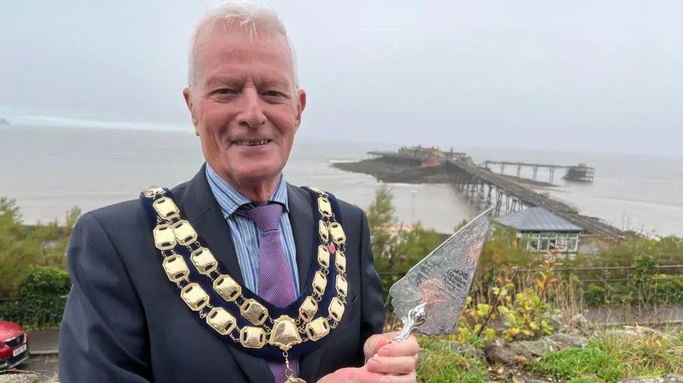 John Crockford-Hawley holding the trowel which his cousin used to lay the pier's foundation stone.