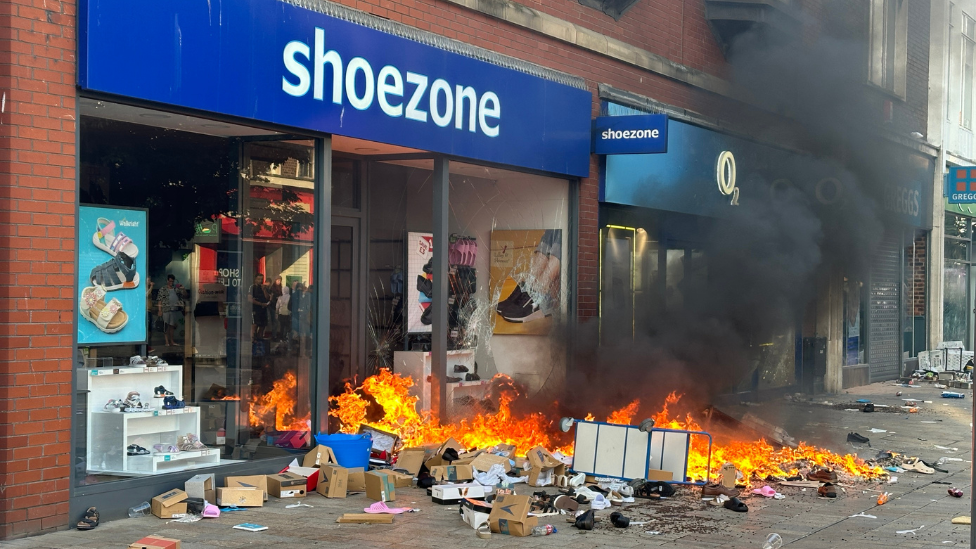 Shoe Zone on fire in Hull city centre, following disorder. Flames come from the doorway, along with black smoke and boxes on the street 