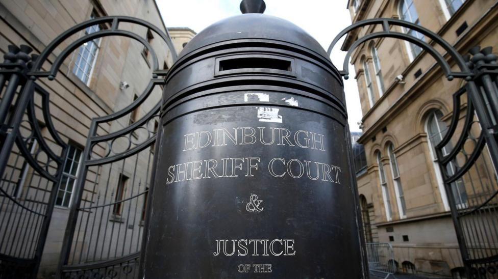 Large sign in front of metal gate bars and sandstone walls that says Edinburgh Sheriff Court