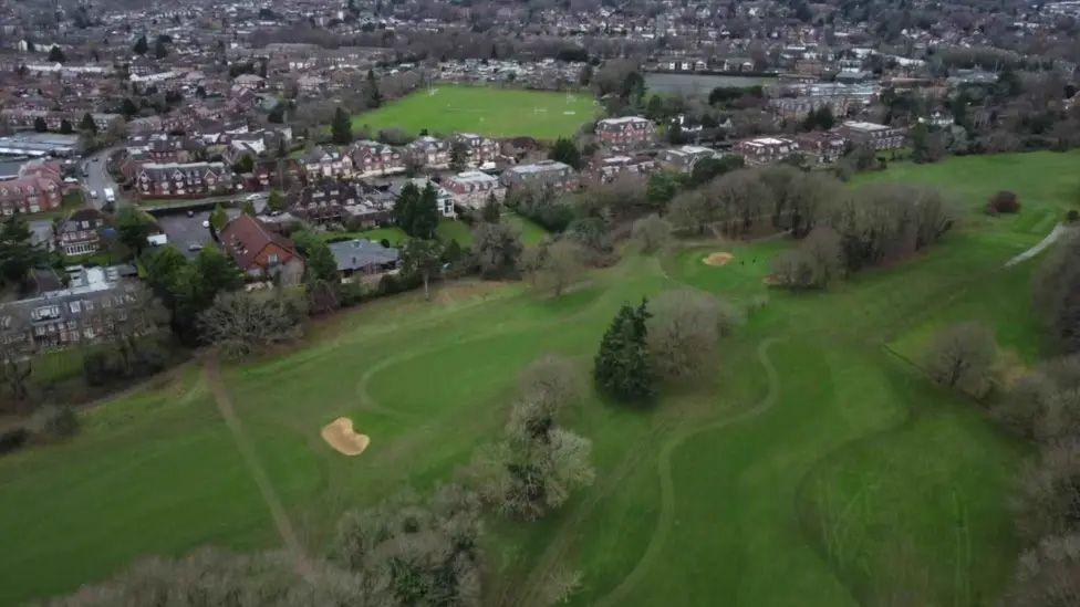 An aerial view of the golf course. You can see the greens and fairways, and trees with bare branches. The course is surrounded by housing. 